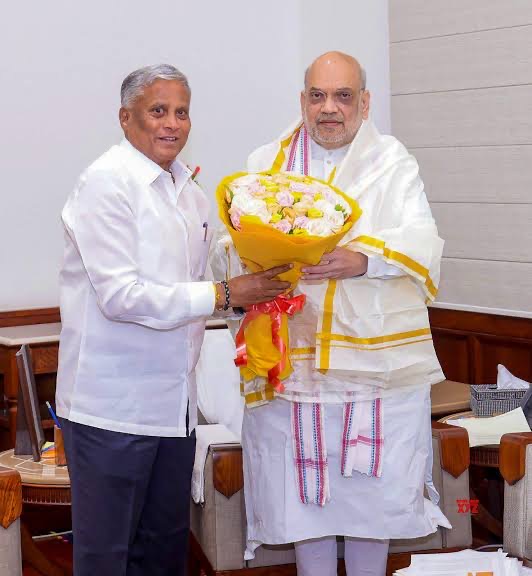V. Somanna presenting a bouquet of pastel flowers to a man wearing a white shawl in an office