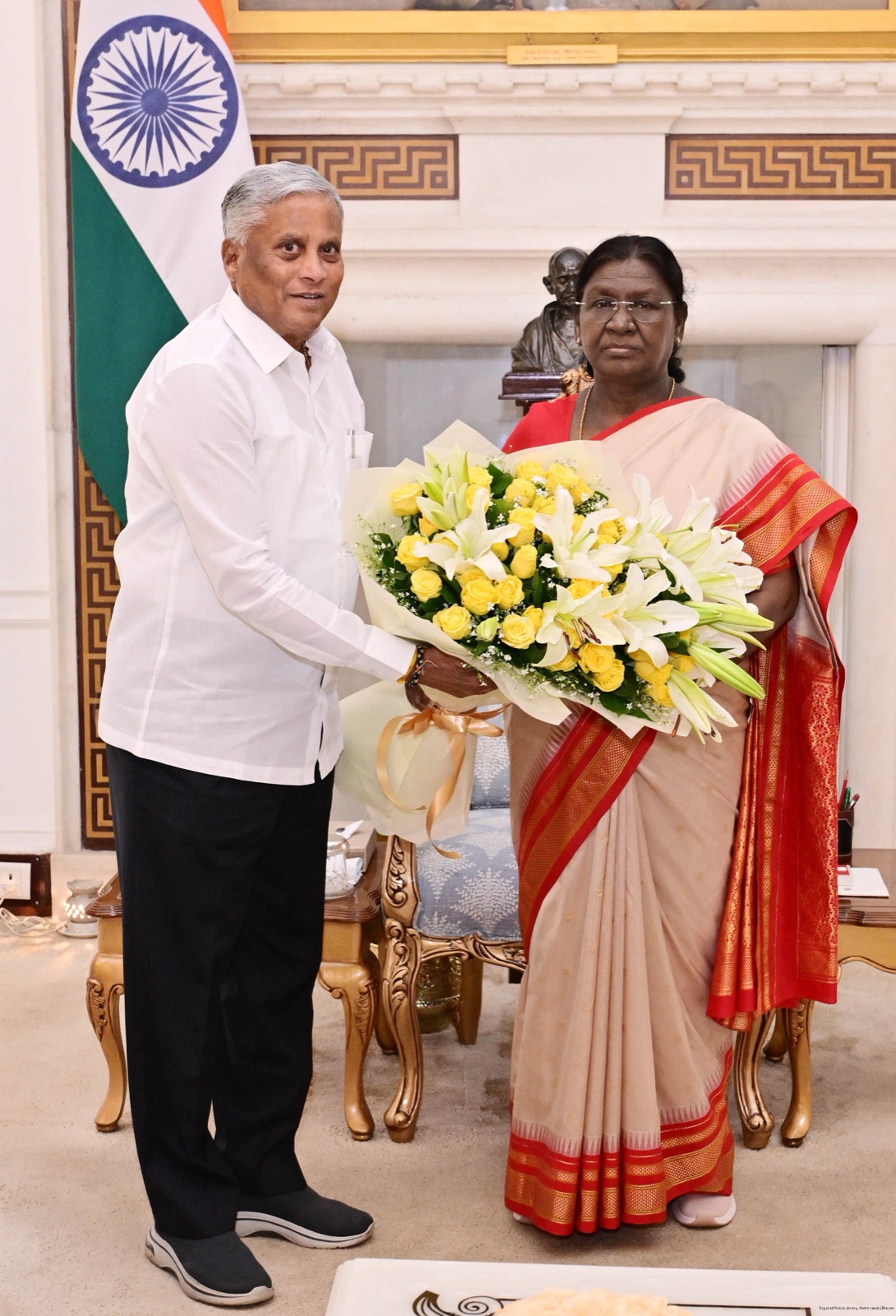 V. Somanna presenting a bouquet of white lilies and yellow roses during a formal courtesy call, beside the national flag