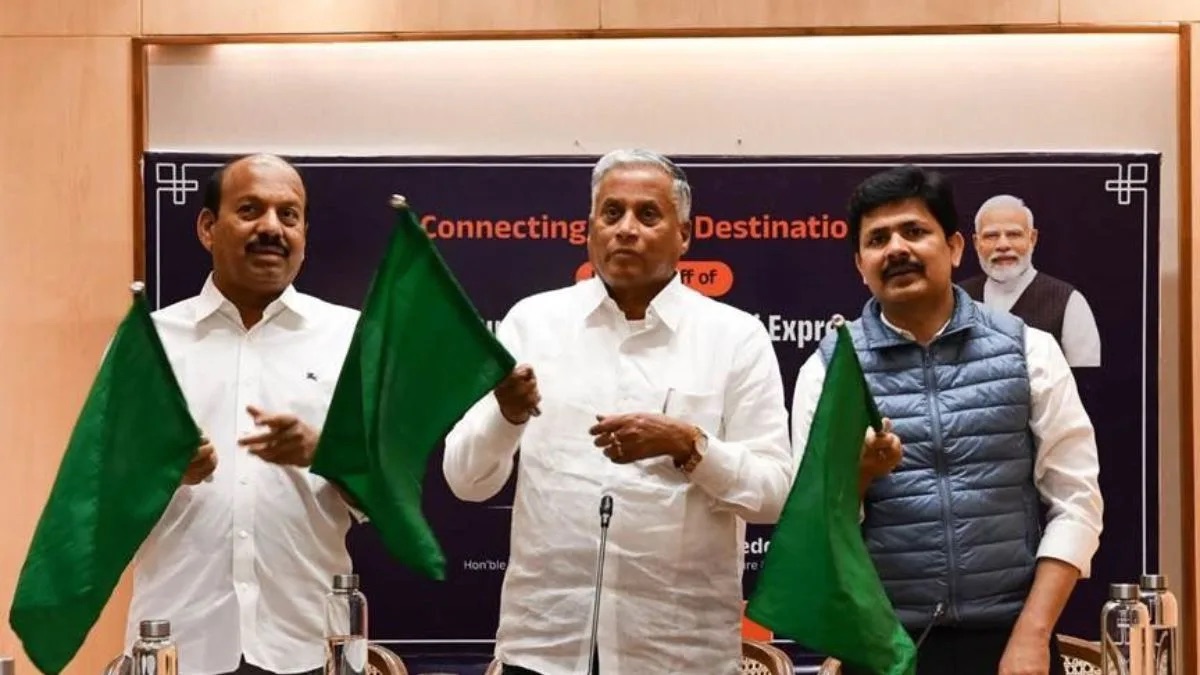 V. Somanna holding a green flag with two other officials at a train flag-off ceremony, in front of a banner reading ‘Connecting Destinations’