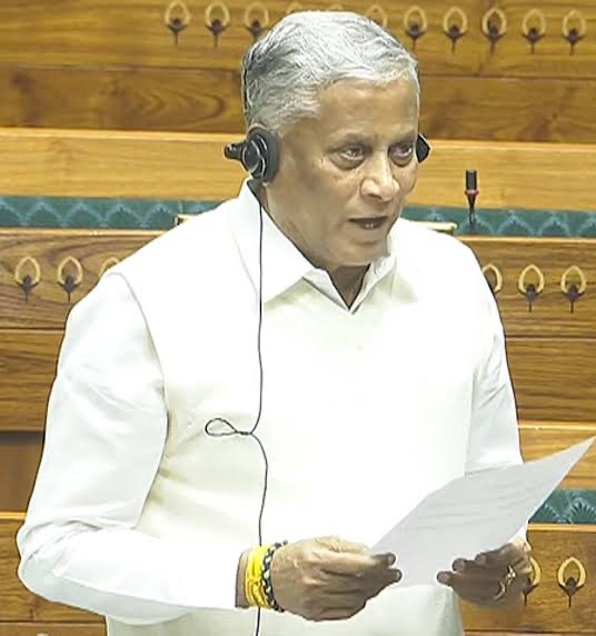 V. Somanna standing in the Lok Sabha chamber wearing an interpretation headset and reading from a sheet of paper