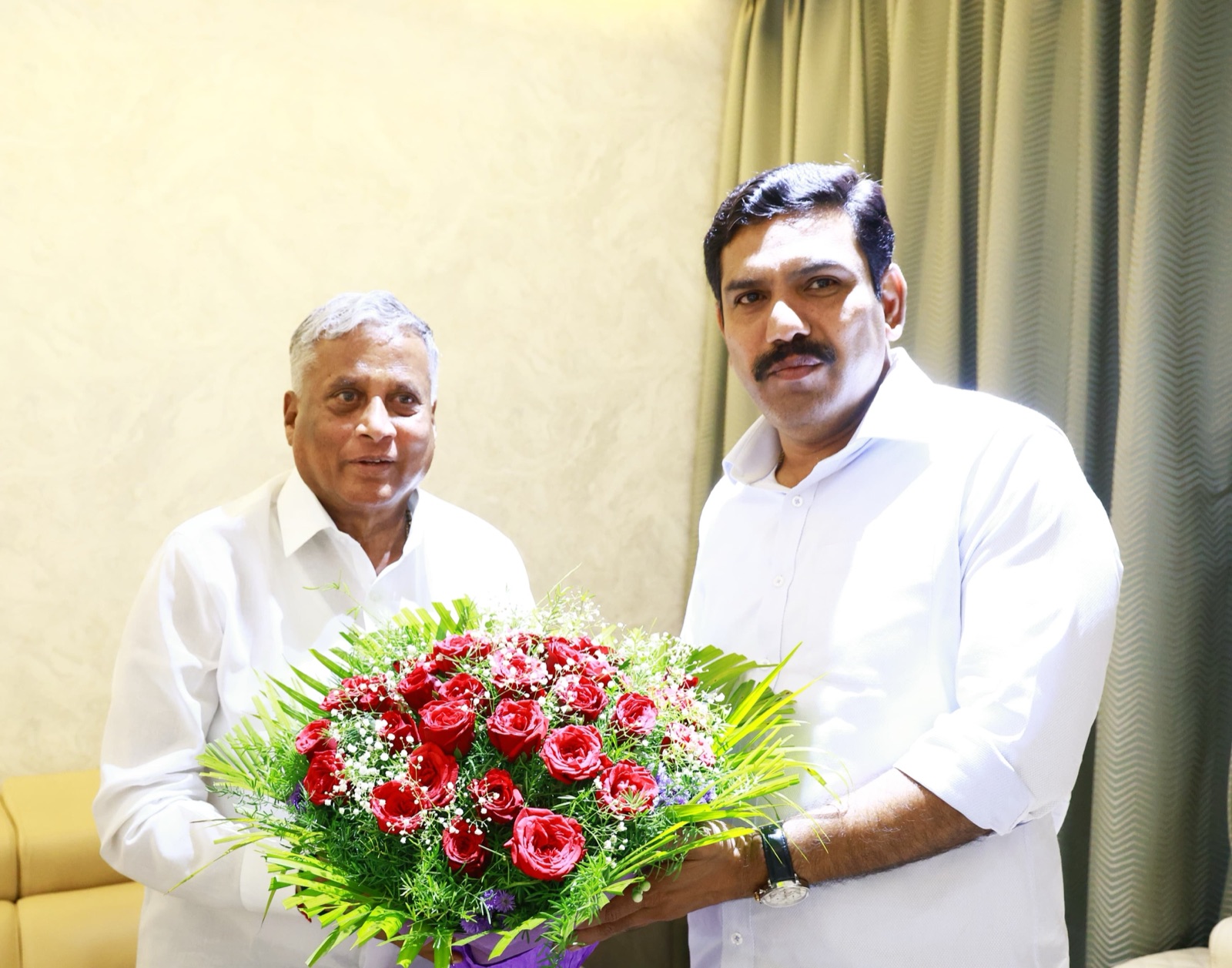 V. Somanna, left, being handed a bouquet of red roses by a man in a white shirt