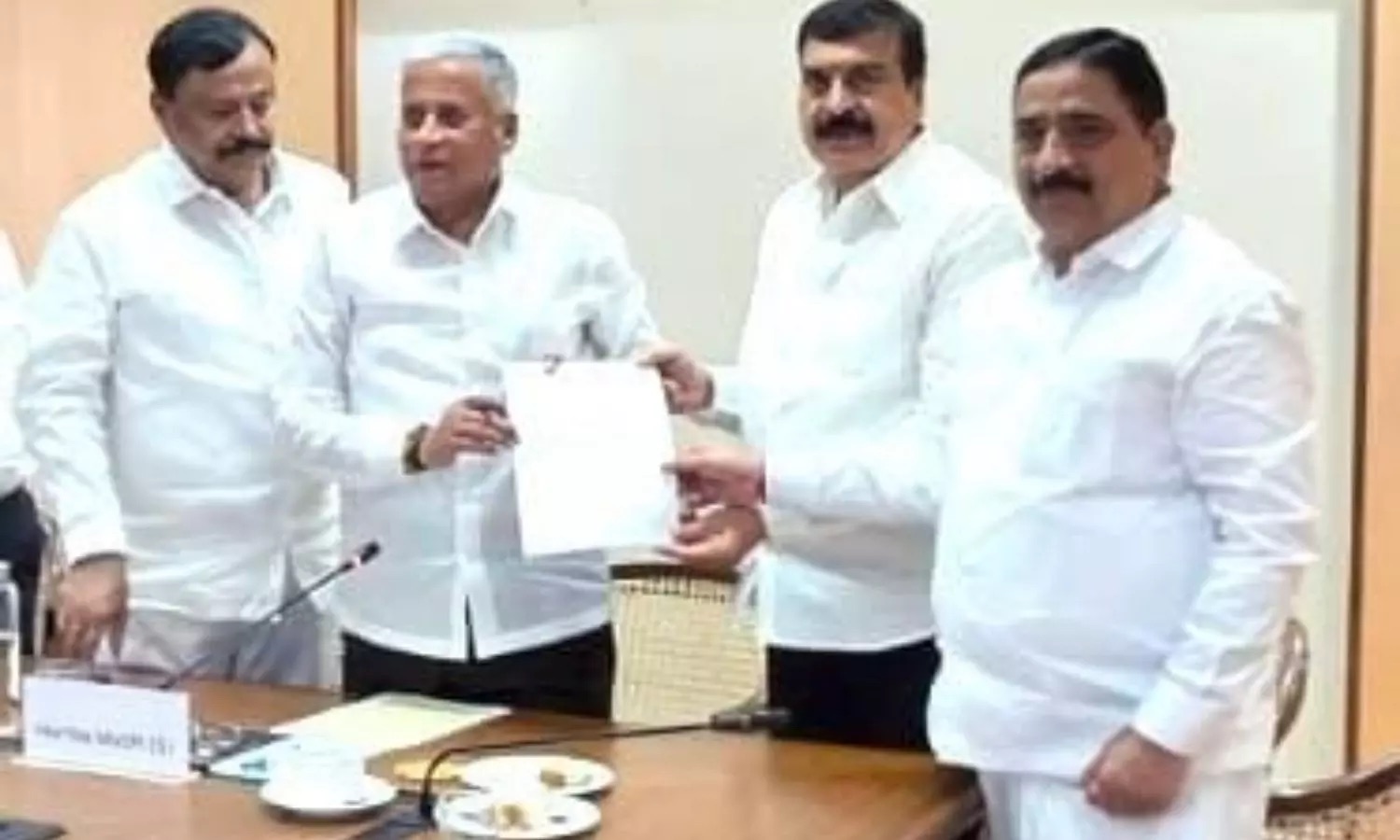 V. Somanna receiving a written memorandum from a man across a meeting table, with two other men beside them
