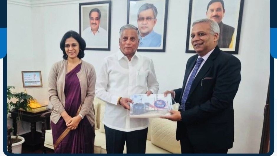V. Somanna, centre, receiving a railway publication from two officials in an office with framed portraits on the wall